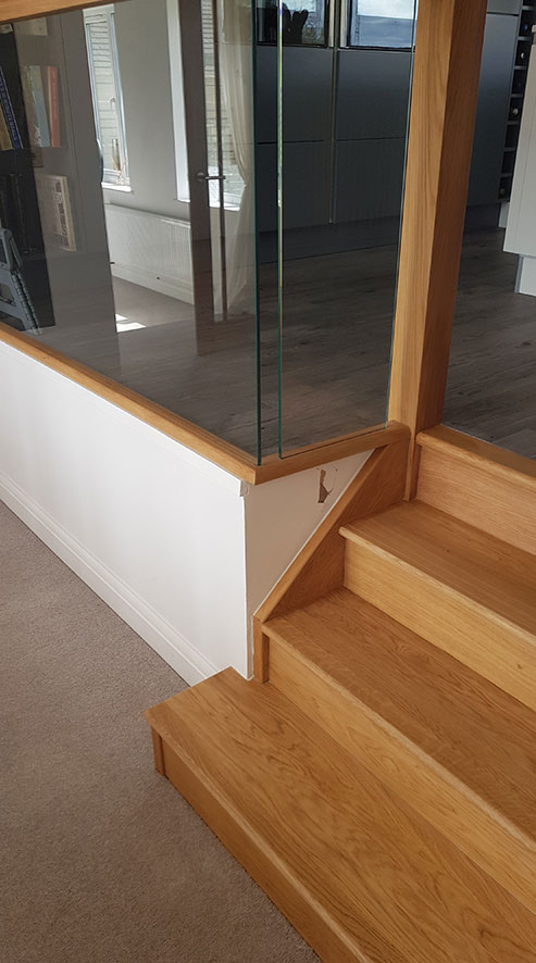 an oak bottom step of a staircase with a glass panel above